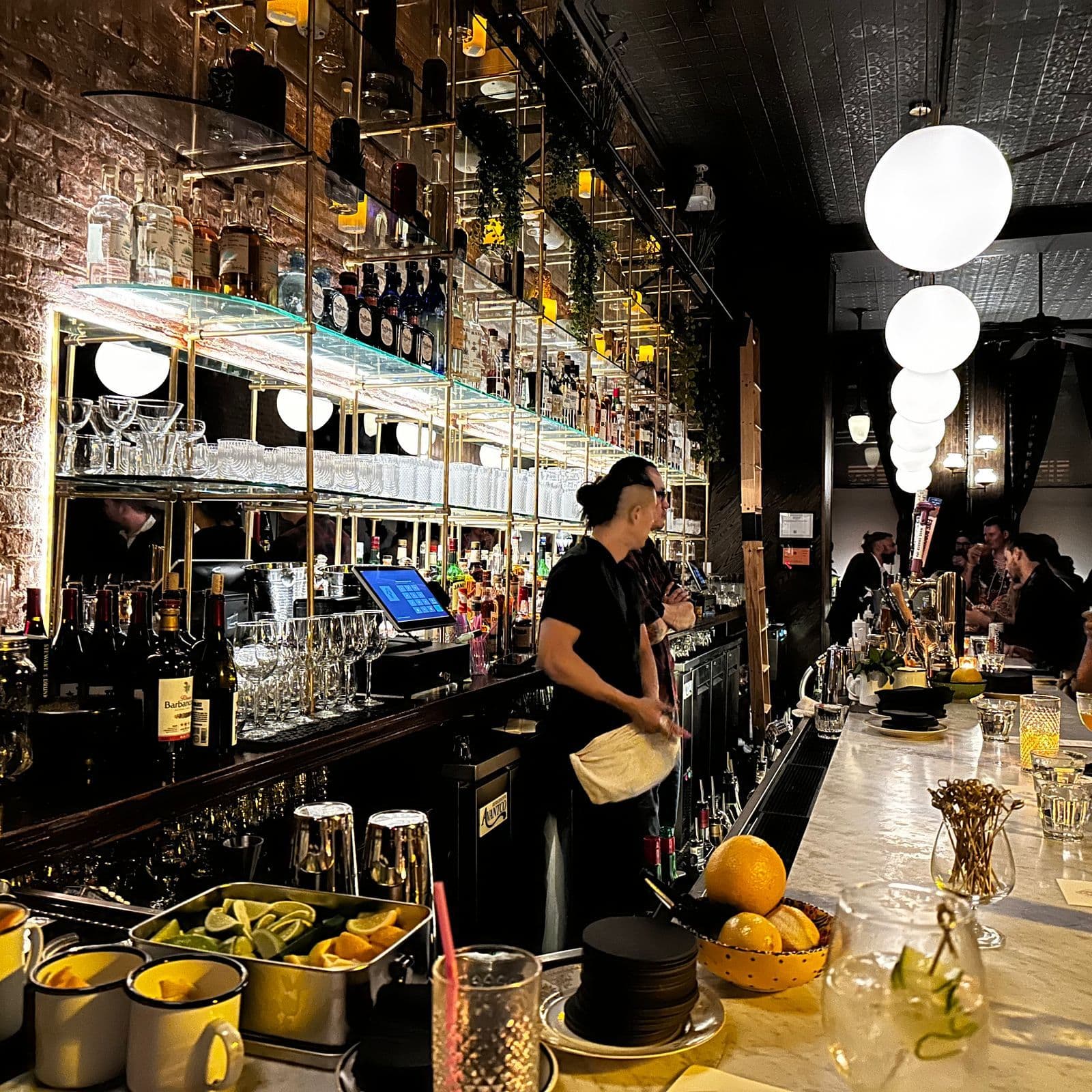 Dimly lit interior of Little More in Tribeca with its long marble bar and towering spirits library